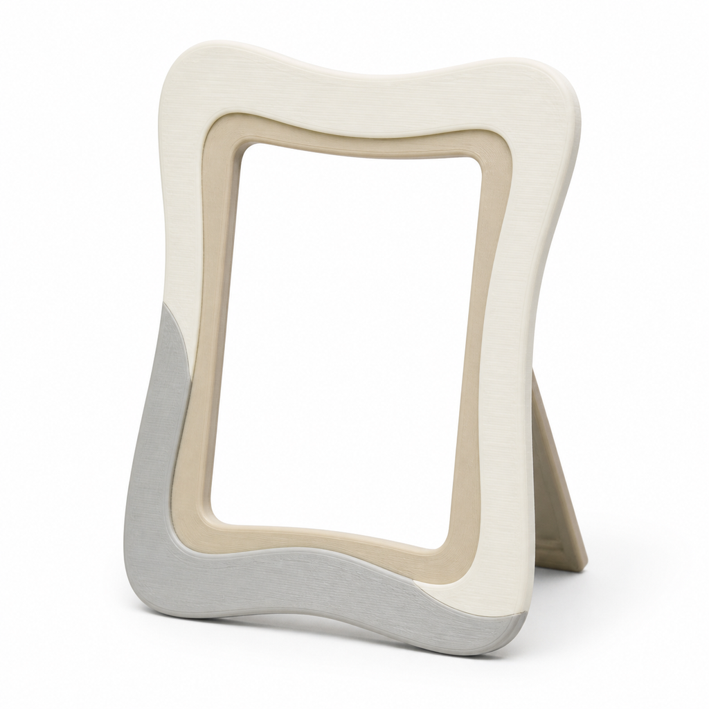Product image of "Standing photo frame with soft wave edges" on white background: photo frame; Basic shape: high-format curved rectangular frame with back support; Design: an organic corrugated outer contour and three-coloured edge segments; Colours: off-white, beige and light grey.