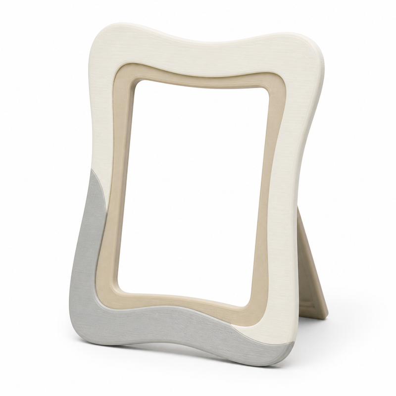 Product image of "Standing photo frame with soft wave edges" on white background: photo frame; Basic shape: high-format curved rectangular frame with back support; Design: an organic corrugated outer contour and three-coloured edge segments; Colours: off-white, beige and light grey.