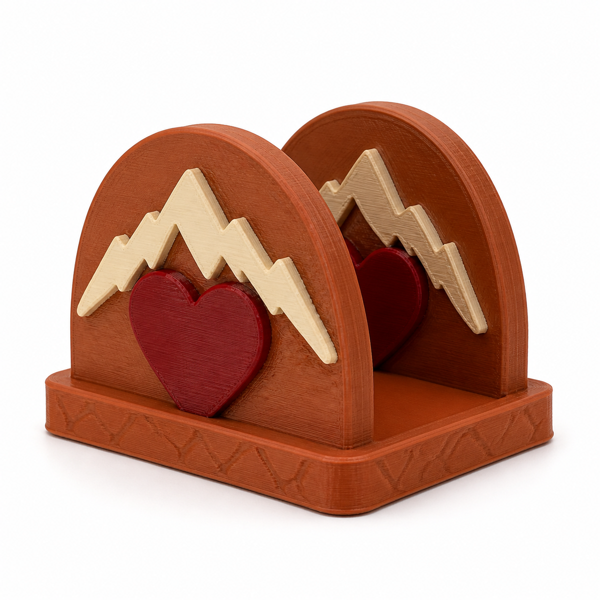 Product illustration of "napkin holder Herzberge" on white background: napkin holder; Basic shape: rectangular foot with two arc-shaped side walls; Design: mountain silhouettes and upstream heart shapes on both sides; Colours: terracotta, Dark red and cream.